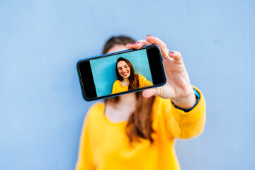 Smiling young woman taking a selfie at a blue wall