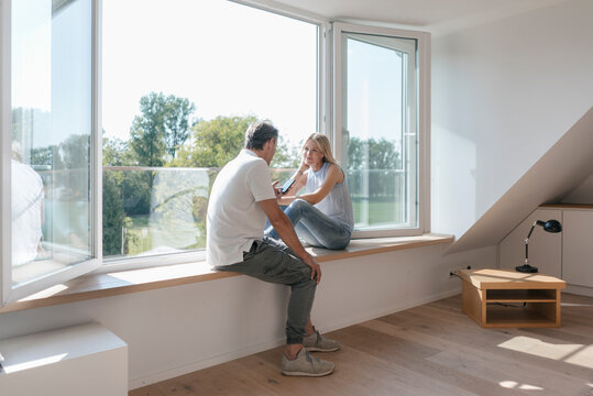 Mature couple with cell phone sitting at the window in empty room