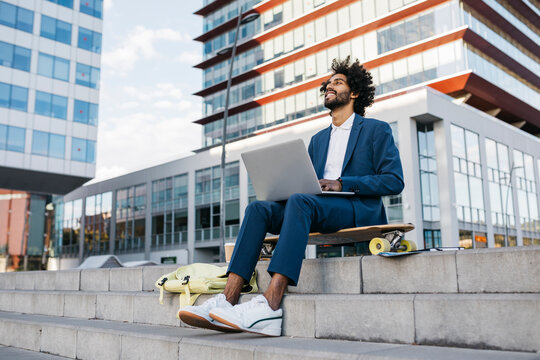 Spain, Barcelona, young businessman sitting outdoors in the city working on laptop