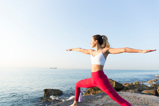 Young woman practicing yoga on the beach, doing warrior pose