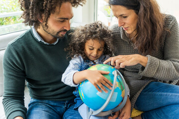 Happy family sitting on couch with globe, daughter learning geography