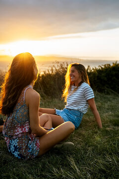 Smiling young woman spending leisure time with friend on field during sunset