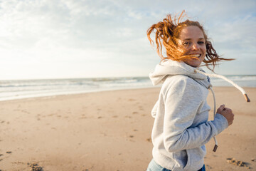 Redheaded woman running on the beach, laughing