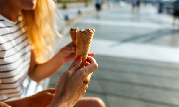Young women eating ice cream while spending leisure time in city on sunny day