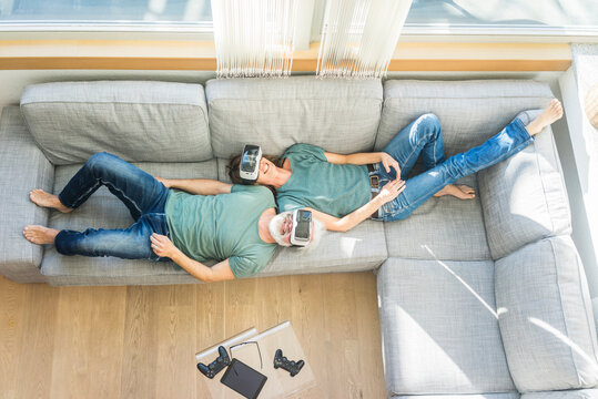 Happy mature couple lying on couch at home wearing VR glasses