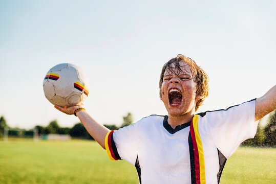Boy wearing German soccer shirt screaming for joy, standing in water splashes