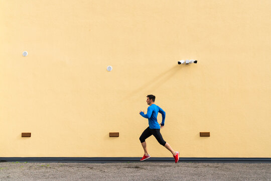 Sportive man running along yellow wall with CCTV camera
