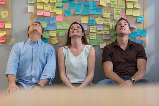 Smiling colleagues sitting in front of wall with sticky notes in office looking up