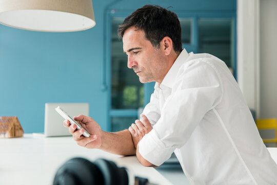 Serious Businessman Looking At Cell Phone In Office