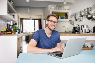Portrait of smiling man using laptop in kitchen at home