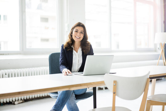 Portrait of happy businesswoman sitting at desk in the office working on laptop