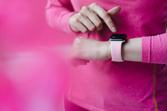 Close-up of woman in pink sportswear adjusting her smartwatch
