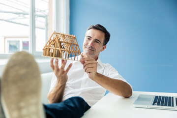 Confident businessman looking at model house in office