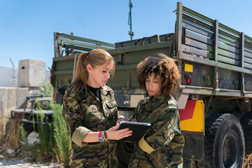 Multi-ethnic female army soldiers discussing over digital tablet at military base on sunny day