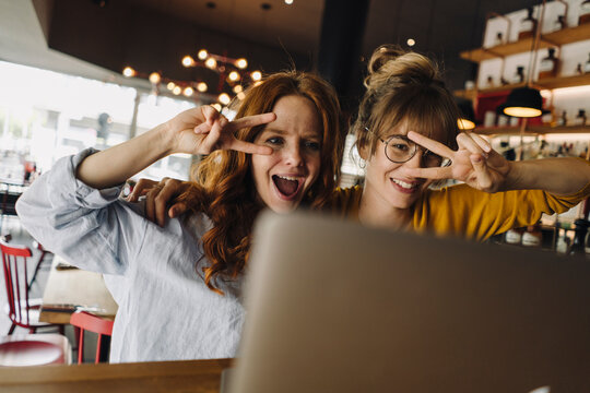 Two playful female friends with laptop in a cafe