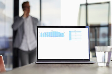 Chart on laptop screen on desk in office with businessman in background