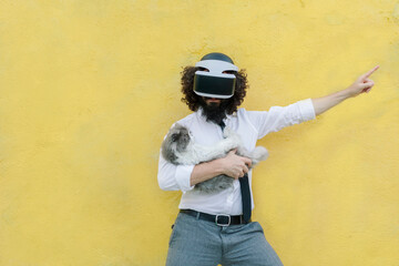 Man wearing virtual reality eyeglasses holding cat while standing against wall