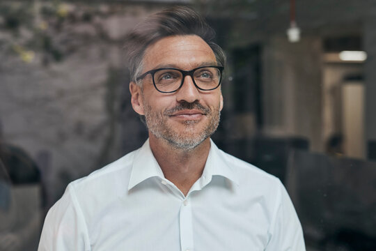 Portrait of smiling man with stubble behind windowpane wearing white shirt and glasses