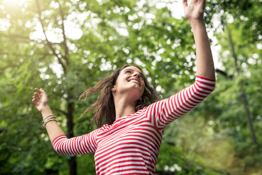 Happy young woman with raised arms dancing in nature