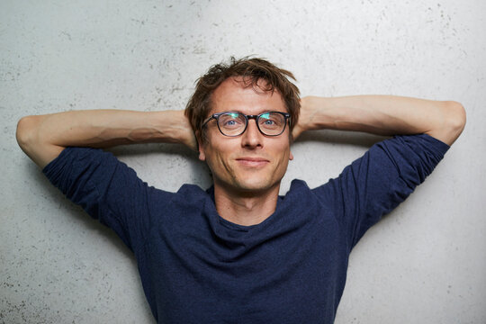 Portrait of smiling man with hands behind head wearing glasses