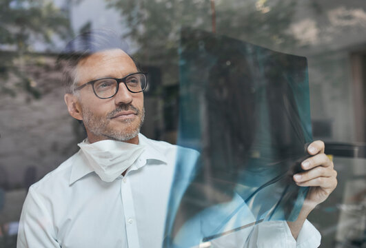 Portrait of radiologist behind windowpane looking at x-ray image
