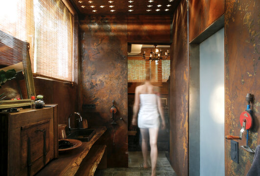 Back view of woman walking in  bathroom with corten steel wall cladding and ceiling light effects