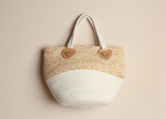 Elegant woman's straw bag hanging on beige background