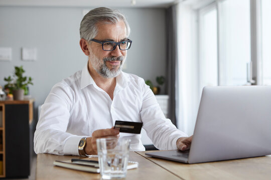 Portrait of content mature man  paying online with credit card at home