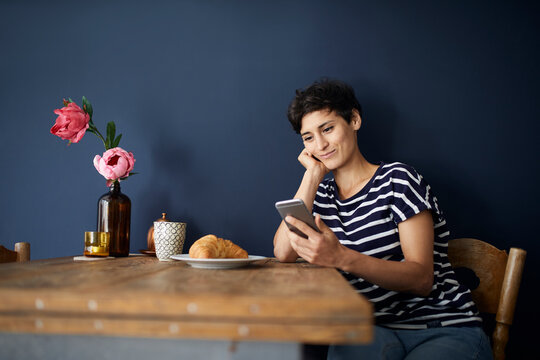 Smiling woman at home sitting at wooden table checking cell phone