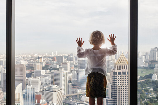 Thailand, Bangkok, little girl looking through window at cityscape