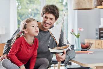 Happy father and daughter playing with model boat at home