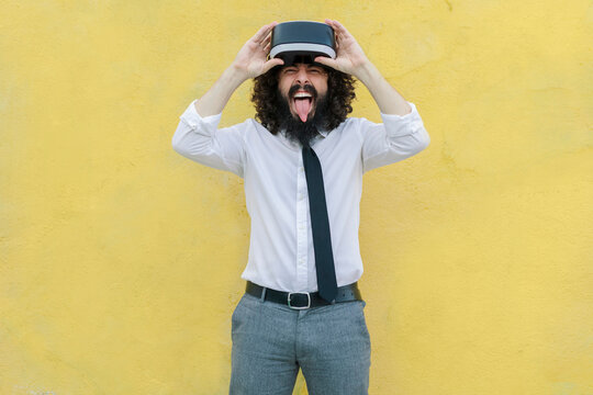 Man teasing with sticking out tongue while removing virtual reality glasses against wall