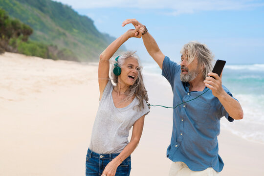 Handsome senior couple with headphones dancing on the beach - Powered by Adobe