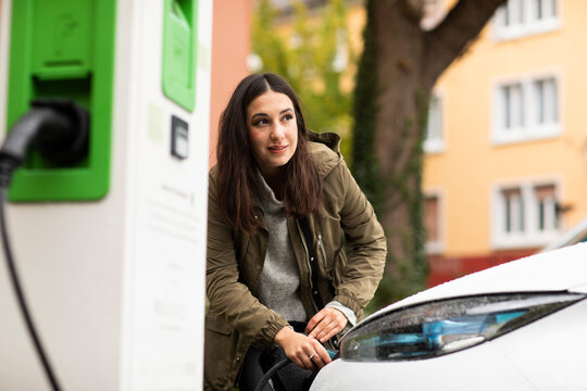 Beautiful woman removing electric plug from car at charging station