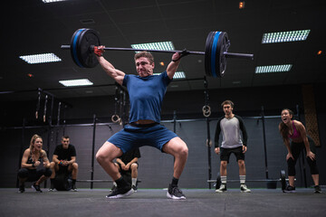 Athletes cheering man picking barbell while standing at gym