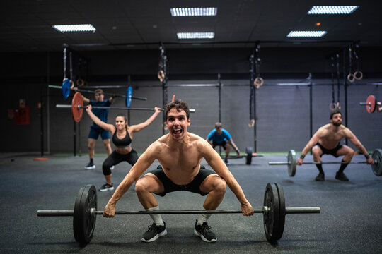 Athletes picking barbell while exercising at gym