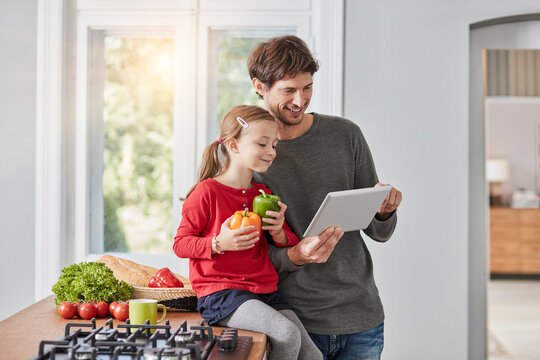 Smiling father and daughter with bell pepper and tablet in kitchen