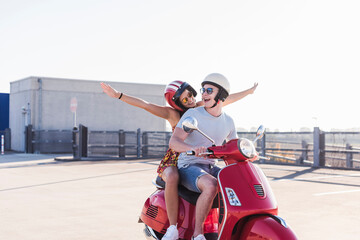 Carefree young couple riding motor scooter on parking level
