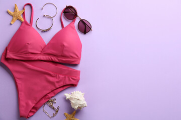 Beautiful pink bikini and beach accessories on lilac background, flat lay. Space for text