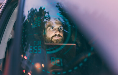 Focused man in car at night surrounded by dashboard projection