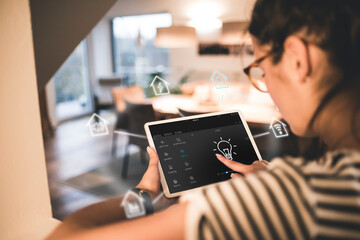 Woman sitting at home, using digital tablet to remote-control his smart home