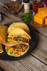 Plate with tasty mexican tacos on rustic wooden table with ingredients for cooking background. Concept of traditional meal. View from above. Recipe book with appetizing food.