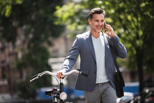 Smiling man on cell phone pushing bike in the city