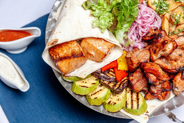 Mixed grill meat fried vegetables and grilled salmon fish fillets decoration in warm dish. Assorted delicious grilled kebab served with herbs on platter. Restaurant menu barbecue plate Bbq party meal
