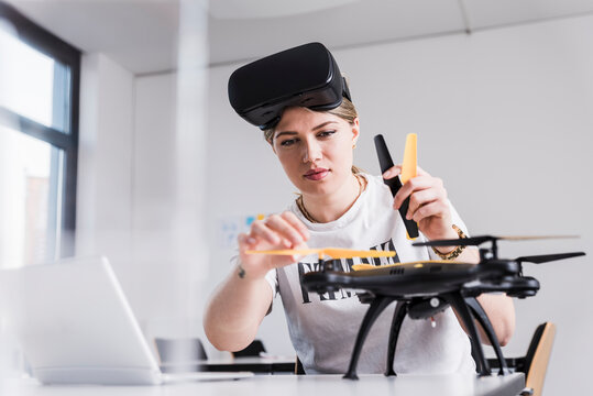 Young woman with laptop and VR glasses at desk examining drone - Powered by Adobe
