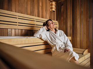 Senior woman with hands behind head relaxing in sauna at health spa