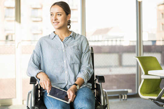 Young businesswoman with tablet sitting in wheelchair in office