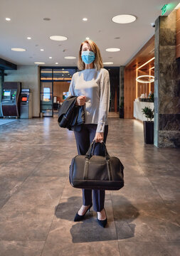 Woman wearing face mask while carrying bag standing in hotel lobby