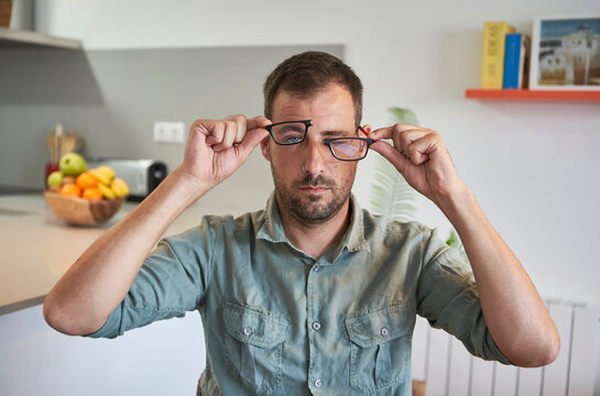 Mid adult man holding broken eyeglasses while sitting at home