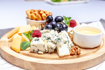 Board with different types of cheese. Cheeses mix set dor blu chedar parmesan brie honey sauce finger bread and grape on wooren palte. Restaurant menu breakfast plate. Healthy snack assortment.